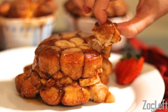 Fingers grabbing a piece of Apple Fritter Monkey Bread from a big plate  garnished with strawberry slices