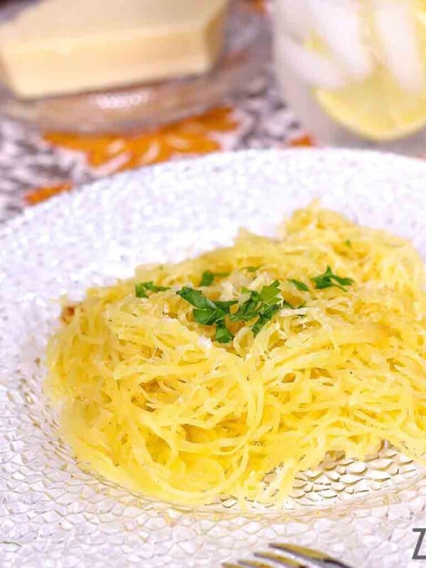 a plate of spaghetti squash topped with chopped parsley next to a glass of lemon water