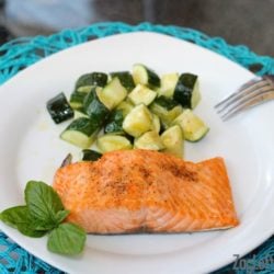 a cooked salmon fillet next to cooked zucchini on a white plate next to fresh basil