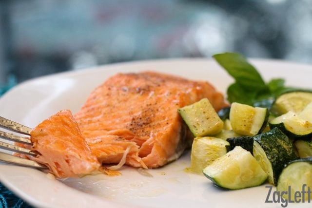 A forkful of salmon fillet on a plate with chopped roasted zucchini.