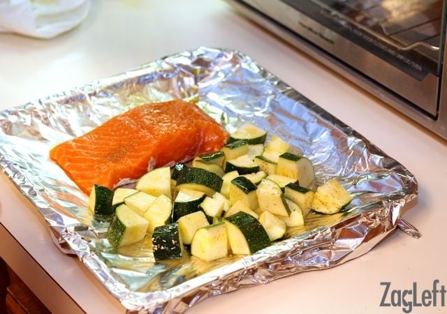 a piece of salmon on a foil lined baking sheet next to diced zucchini.