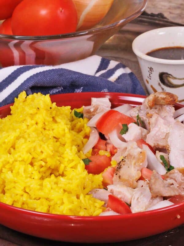 chicken and rice in a red bowl next to a bowl of soy sauce.
