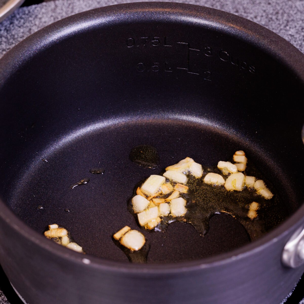 minced garlic sauteeing in a small saucepan on a stove.