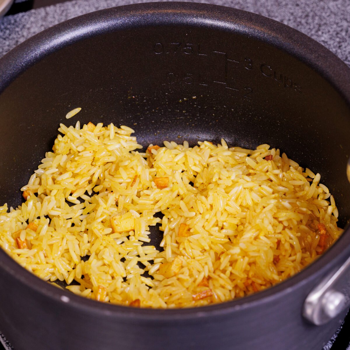 rice sauteeing with oil and turmeric making the color golden in a saucepan.