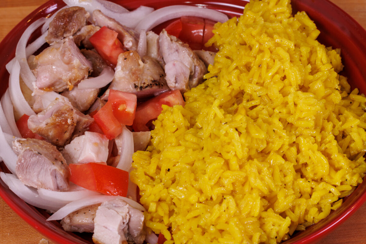 Golden rice in a red bowl next to diced chicken and onions.