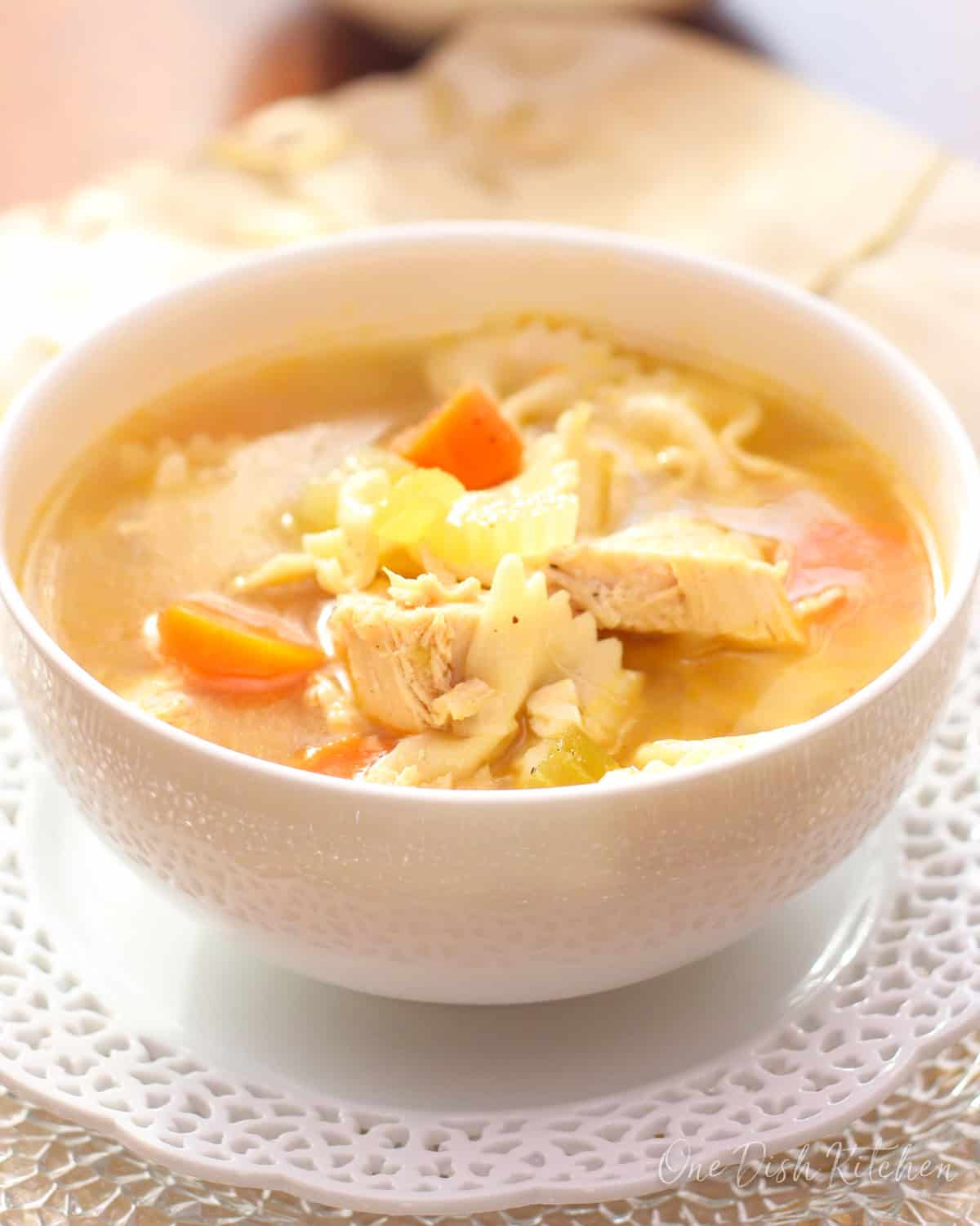 A bowl of chicken noodle soup with another bowl in the background.