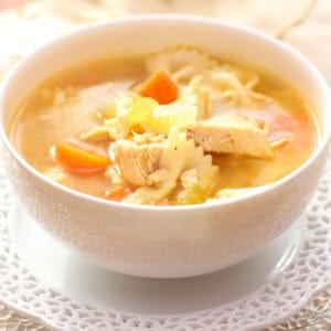 A bowl of chicken noodle soup with another bowl in the background.