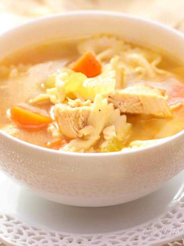 A bowl of chicken noodle soup with another bowl in the background.