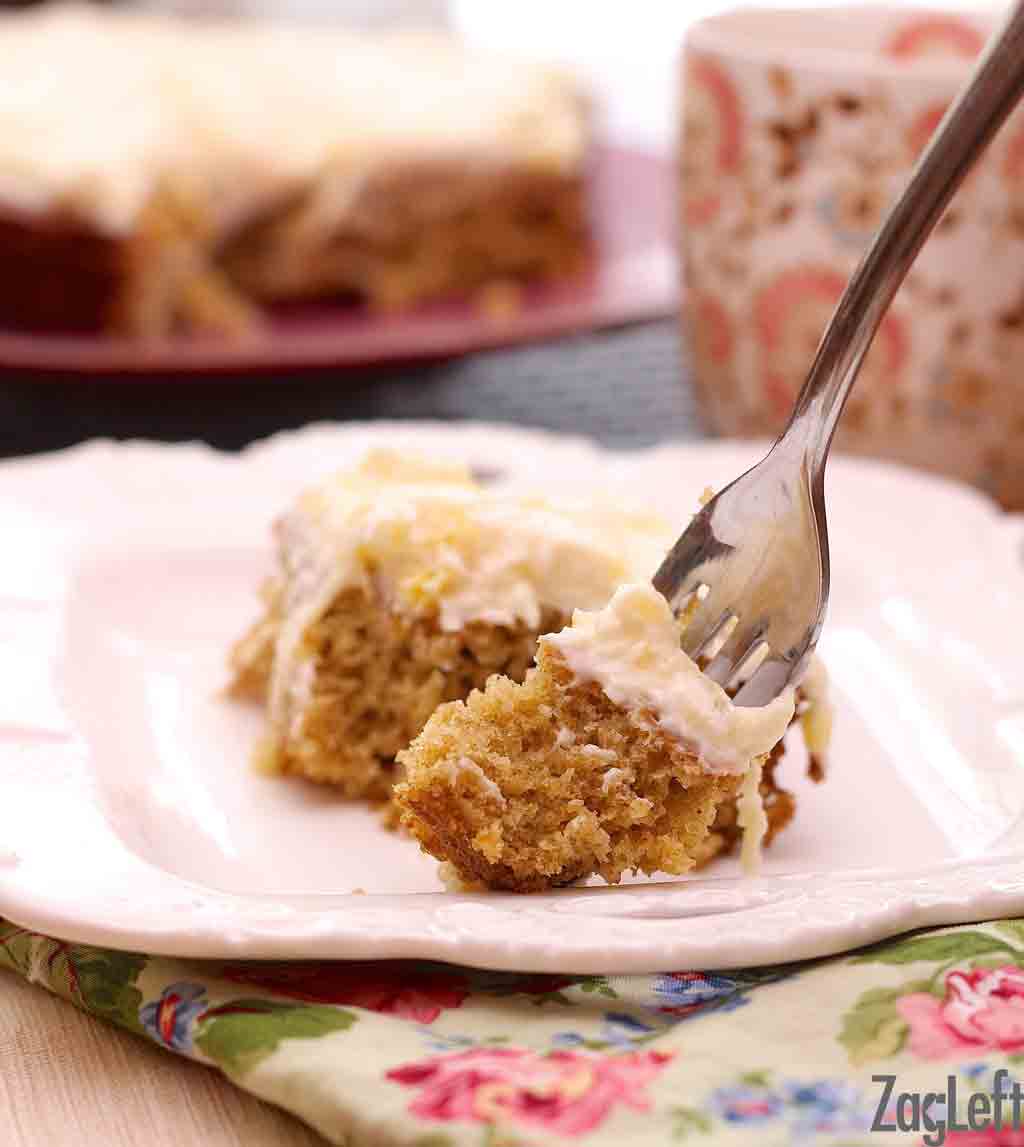 A closeup of a fork in a piece of pineapple oat cake plated on a floral cloth napkin.