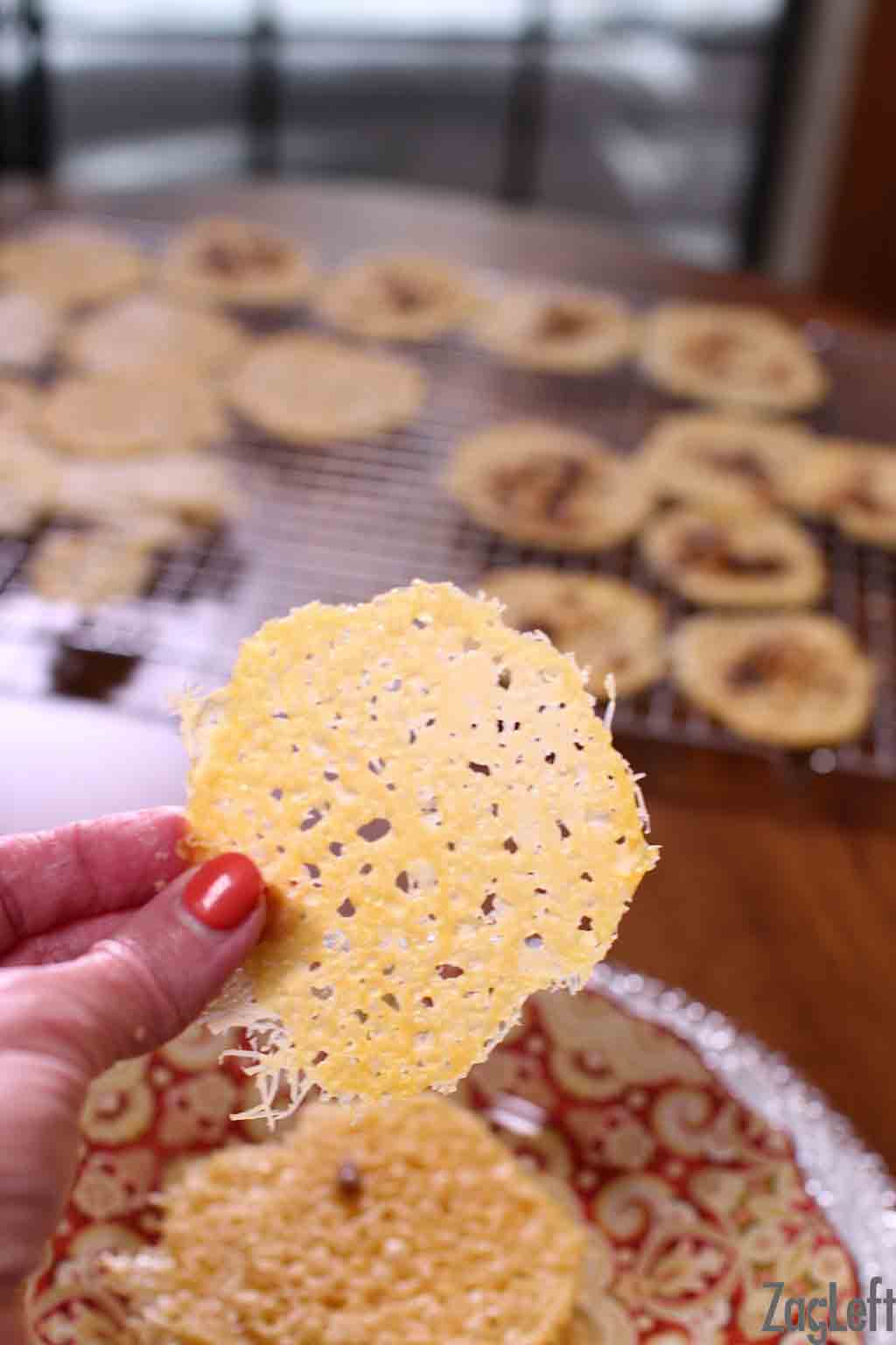 A closeup of Parmesan Cheese Crisps with a cooling rack of crisps in the background.