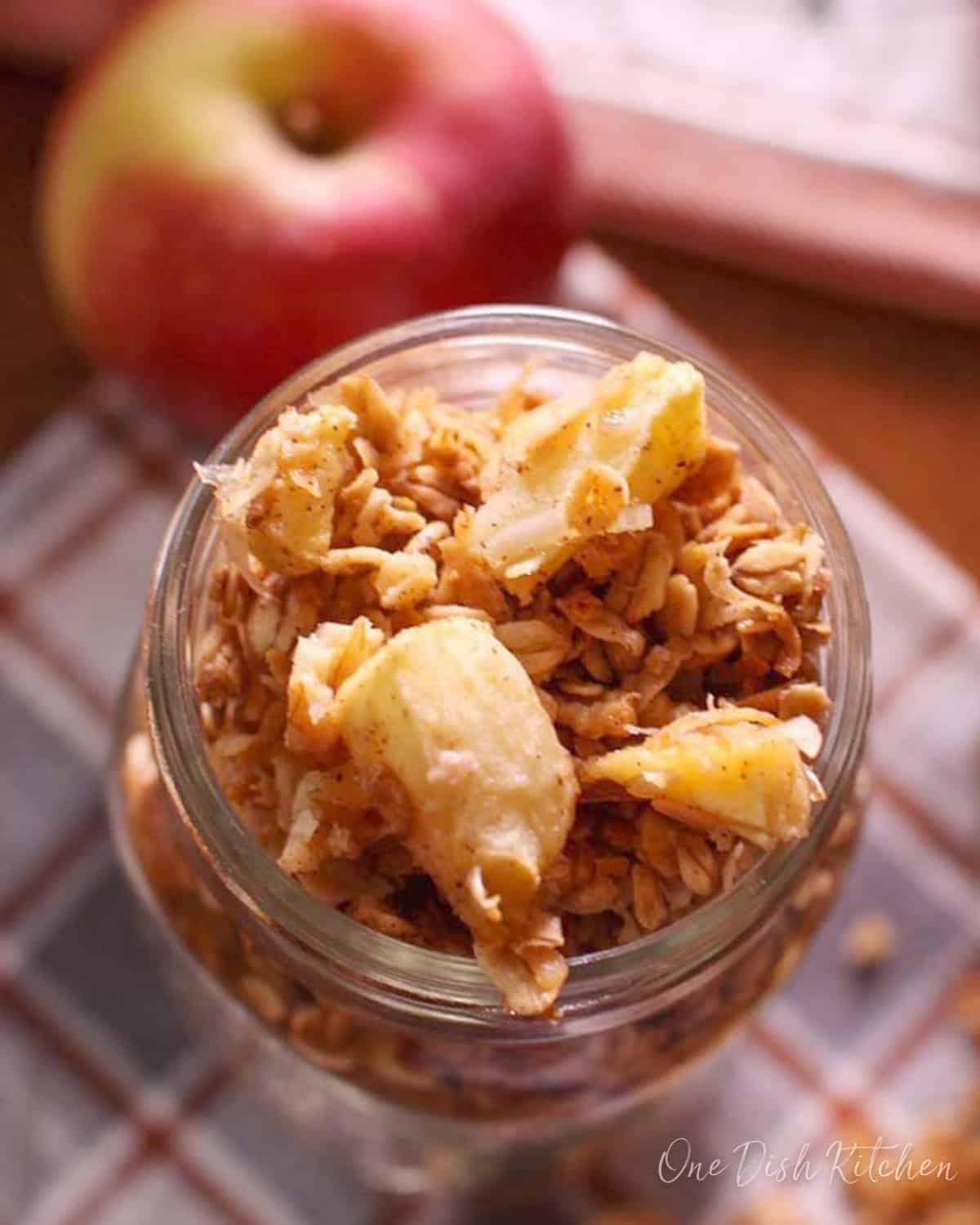 a small jar of homemade apple granola on a table next to a fresh apple.
