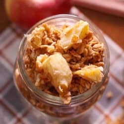 a small jar of homemade apple granola on a table next to a fresh apple.