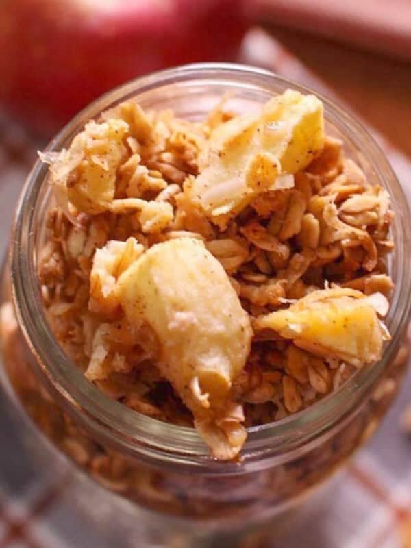 a small jar of homemade apple granola on a table next to a fresh apple.