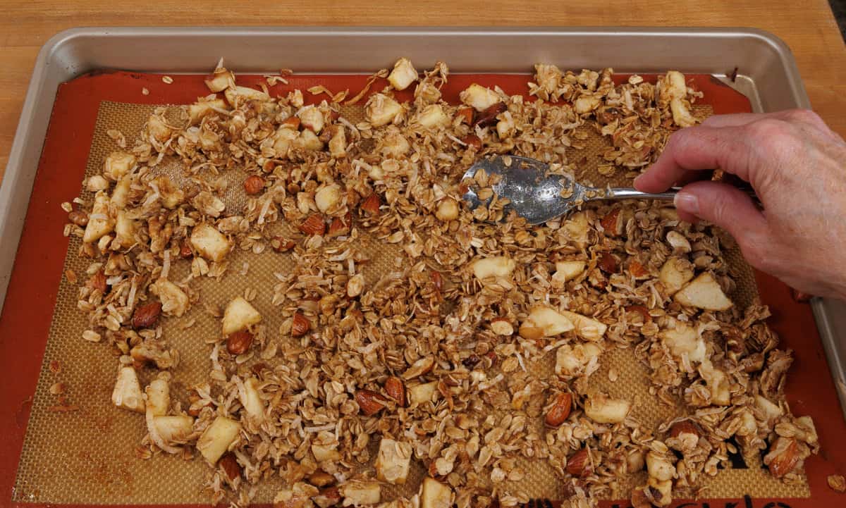 stirring unbaked granola on a sheet pan.