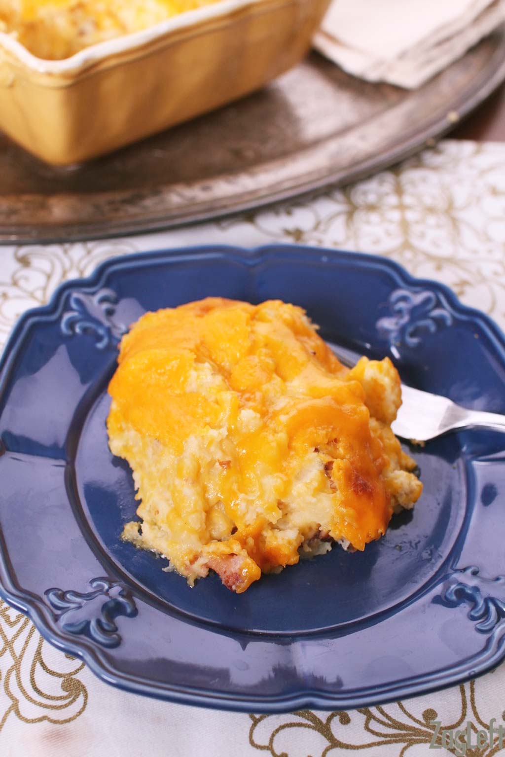 A close up of a slice of Twice Baked Potato Casserole on a small blue plate with a fork 