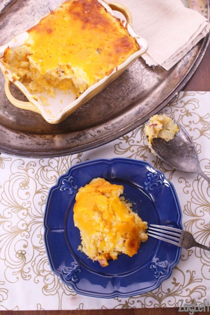 A slice of Twice Baked Potato Casserole on a small blue plate with a fork next to a metal tray holding the casserole in a baking dish 