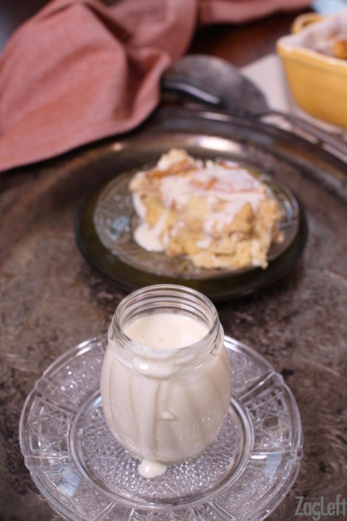 a jar of whiskey sauce with a slice of bread pudding in the background.