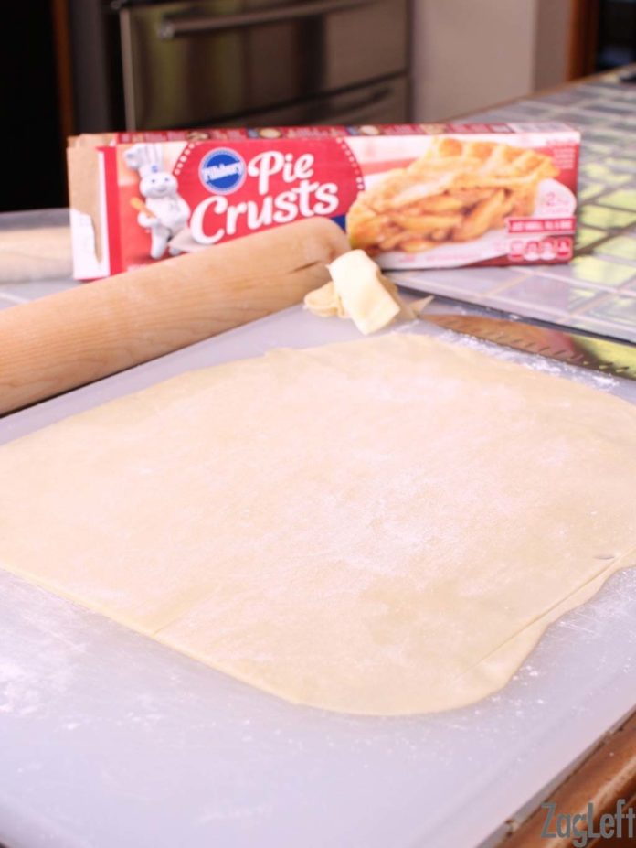 Refrigerator dough rolled out with rolling pin on large cutting board.