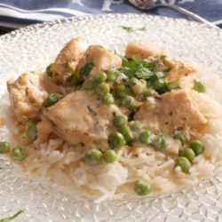chicken fricassee with peas over rice on a white plate