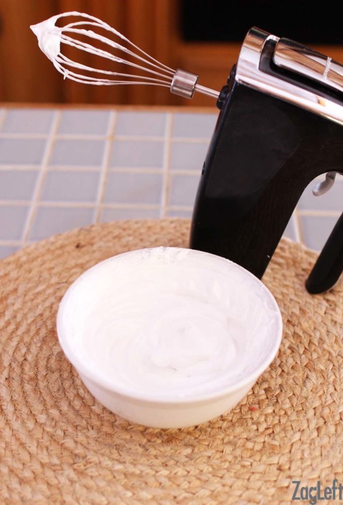 Whipped egg whites and sugar in a bowl with a handheld mixer 