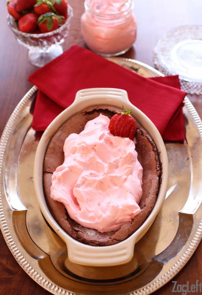Overhead shot of Gluten Free Chocolate Cake topped with strawberry whipped cream in a baking dish on a metal tray next to a small jar of strawberry whipped cream and a small bowl of strawberries