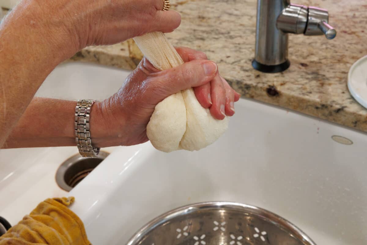 squeezing water or whey from paneer wrapped in cheesecloth over a sink.