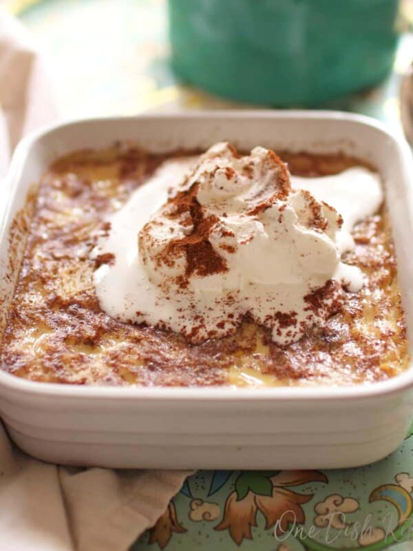 Baked rice pudding topped with whipped cream and ground cinnamon in a small baking dish on a tray.