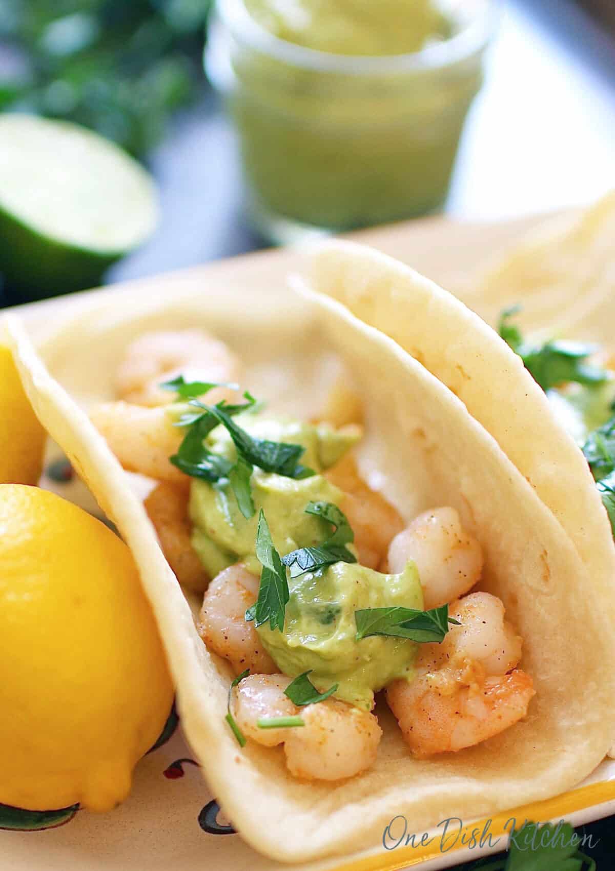 one shrimp taco topped with avocado sauce and chopped cilantro on a plate