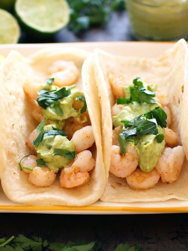 two shrimp tacos with taco sauce on a plate next to lemons and limes