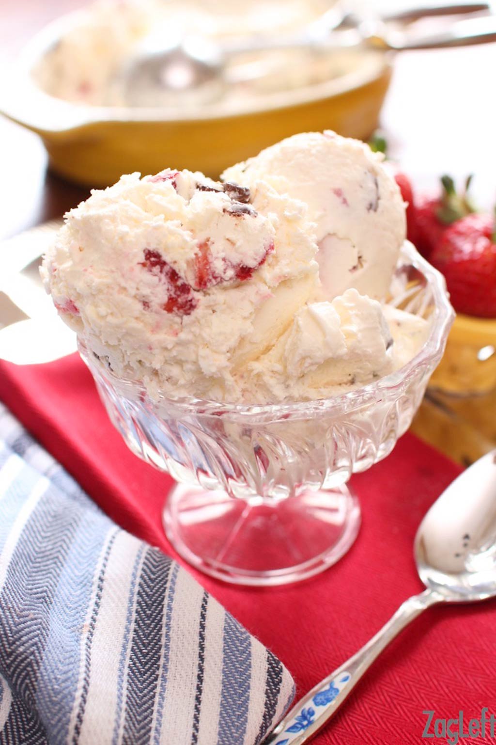 Strawberry ice cream in a dessert glass on a red cloth napkin next to a spoon 
