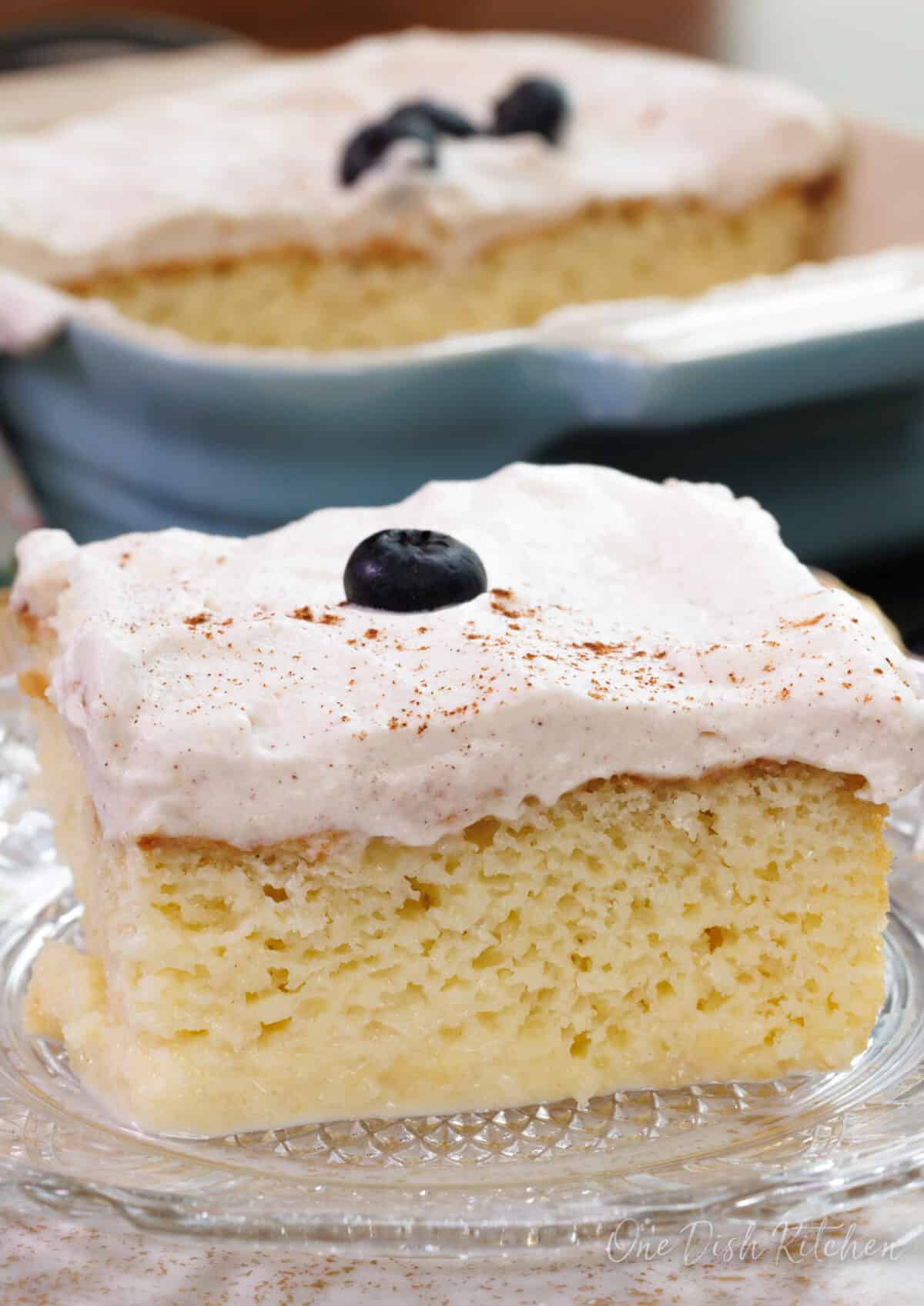 a slice of tres leches cake topped with a blueberry on a white plate.