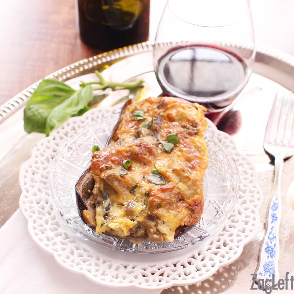 Twice baked eggplant on a glass plate with fork and a glass of red wine all on a metal tray.