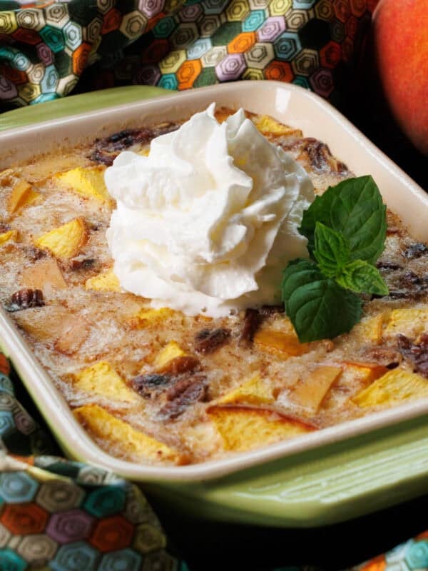 a small peach rice pudding in a green baking dish topped with whipped cream and fresh mint.