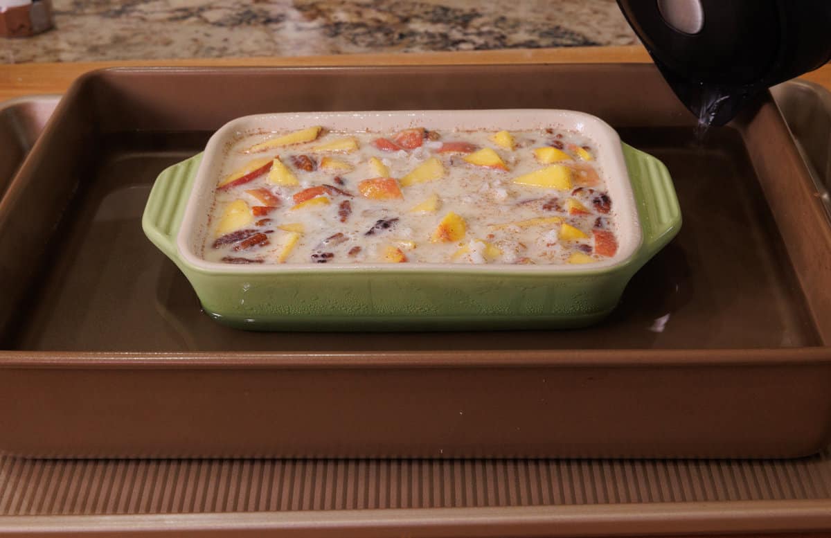 a rice pudding with peaches in a small baking dish in a water bath