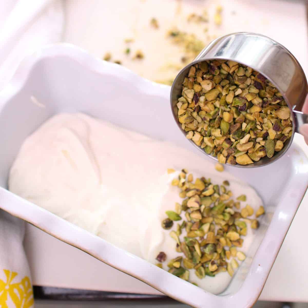 pouring pistachios into ice cream in a loaf pan.