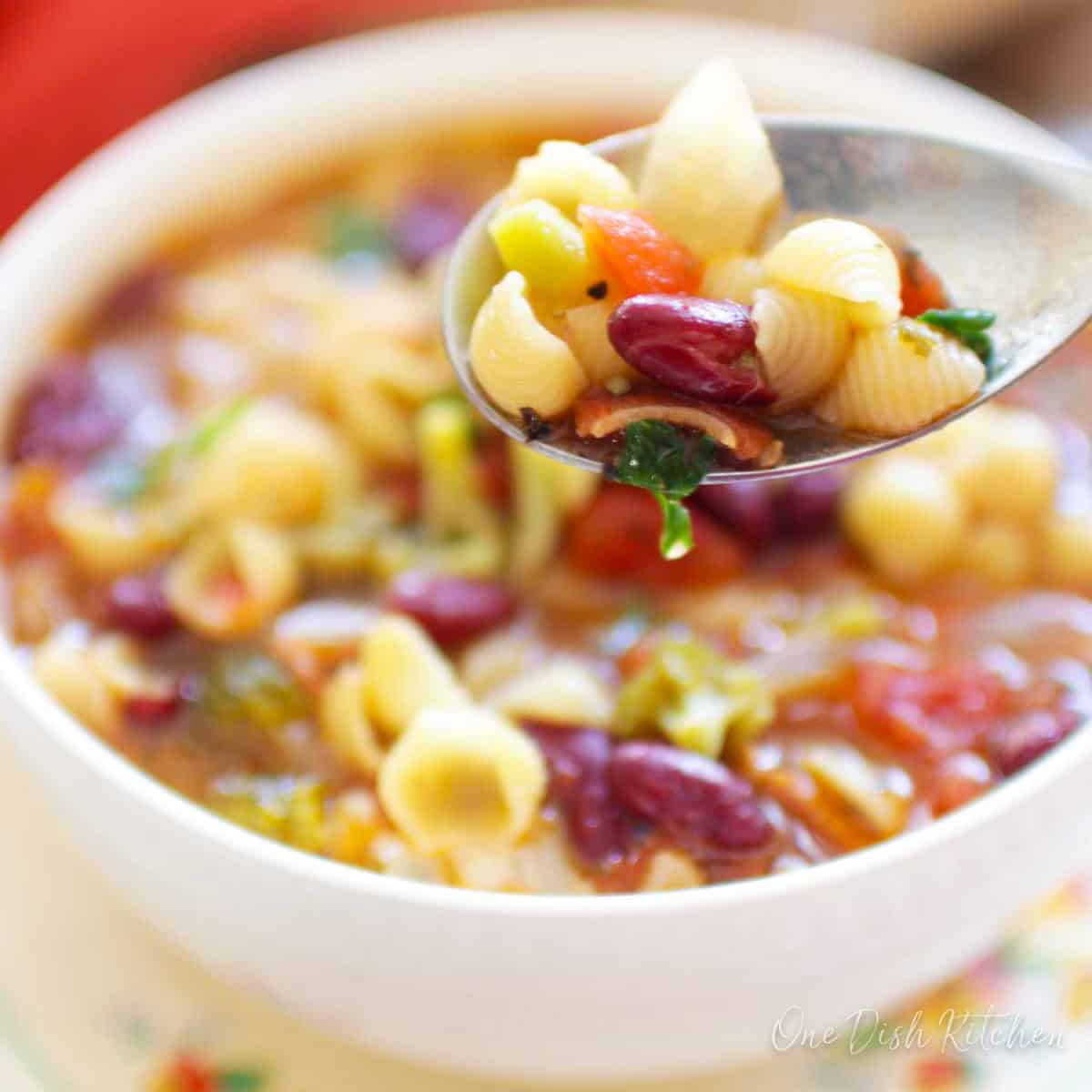 a single serving of minestrone soup in a bowl with a spoon on the side.