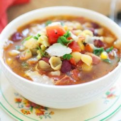 a white bowl filled with minestrone soup topped with shaved parmesan cheese