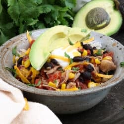 chicken burrito bowl on a silver tray next to fresh cilantro and an avocado.