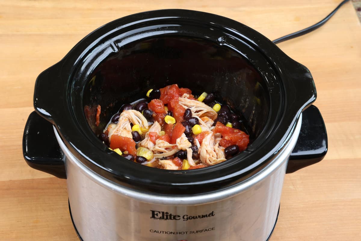 shredded chicken, tomatoes, beans, and corn in a slow cooker.