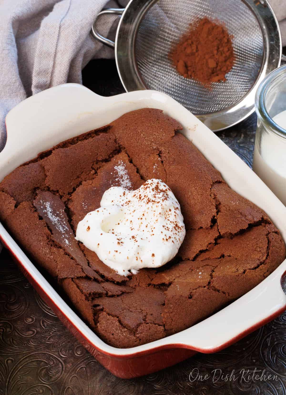 a chocolate flourless cake topped with whipped cream and a dusting of cocoa powder.