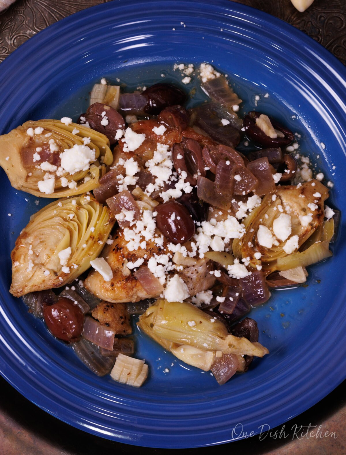 an overhead view of skillet chicken with artichokes and olives on a blue plate.