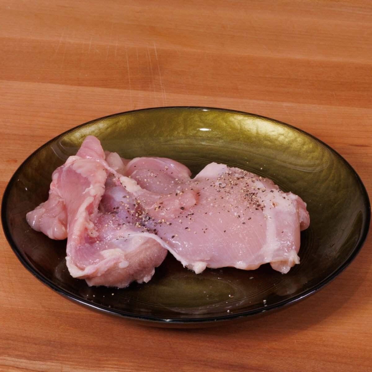 one raw chicken thigh on a green plate.
