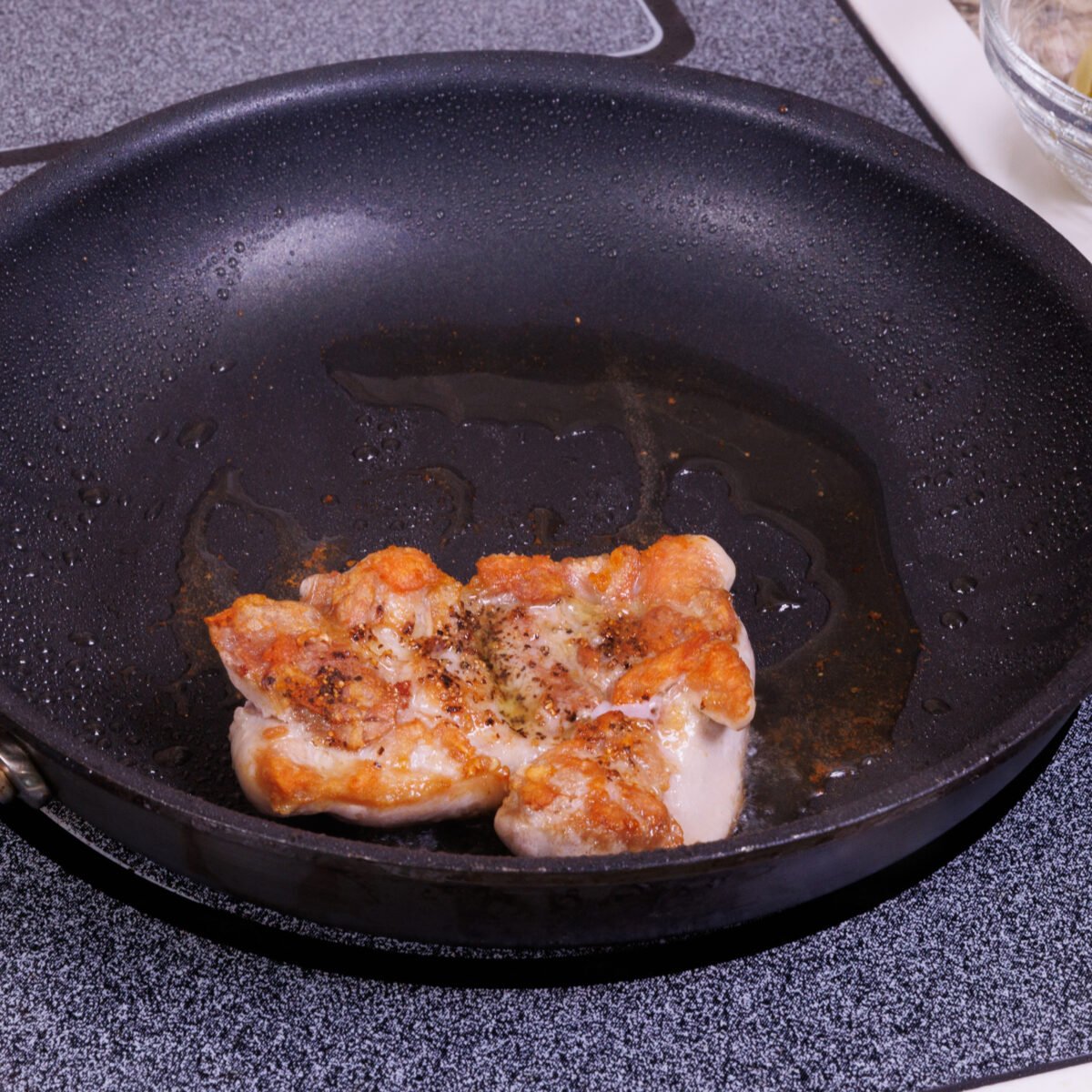 one cooked chicken thigh in a black non stick skillet.