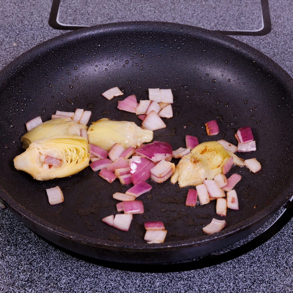 sliced artichokes and red onions cooking in a skillet.