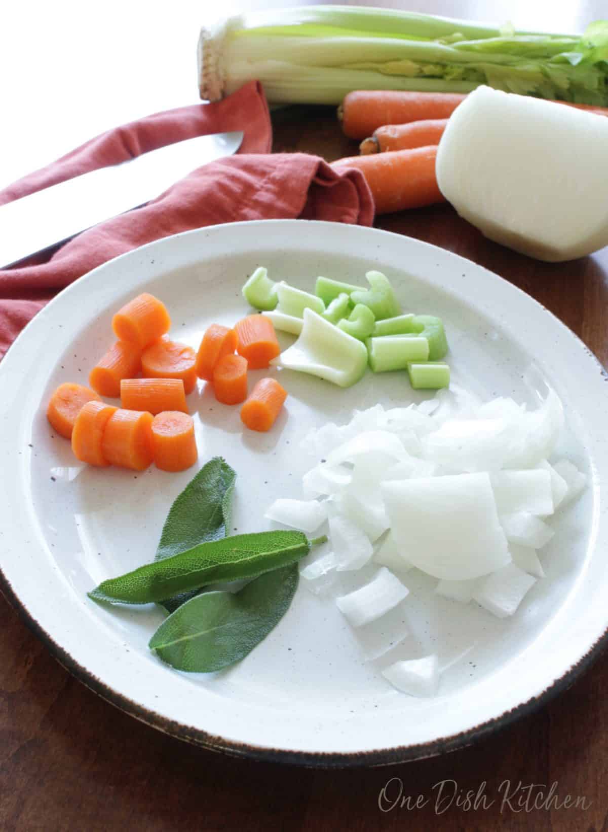a plate filled with sage leaves, carrots, celery, and chopped onions.