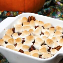 a small sweet potato casserole topped with marshmallows and pecans next to a small pumpkin.