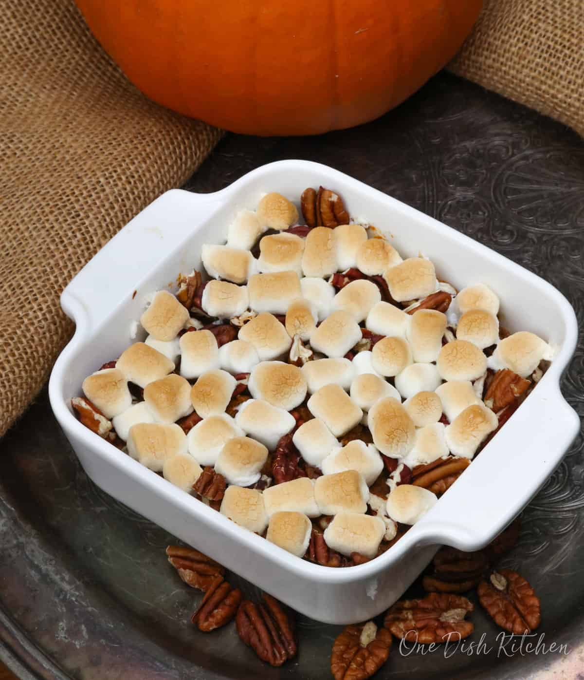 an overhead picture of a mini sweet potato casserole with marshmallows on a silver tray next to a handful of pecan halves.
