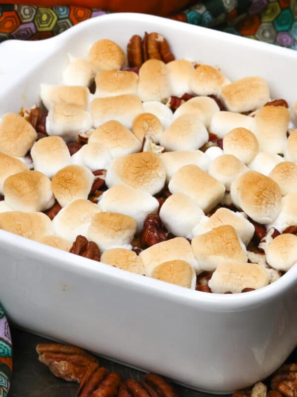 a small sweet potato casserole topped with marshmallows and pecans next to a small pumpkin.