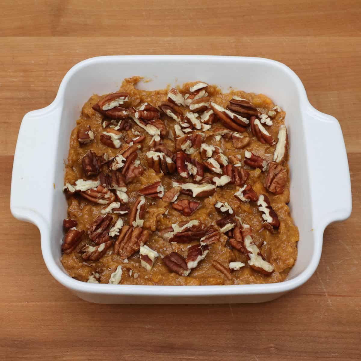 an unbaked sweet potato casserole topped with pecans on a wooden counter.
