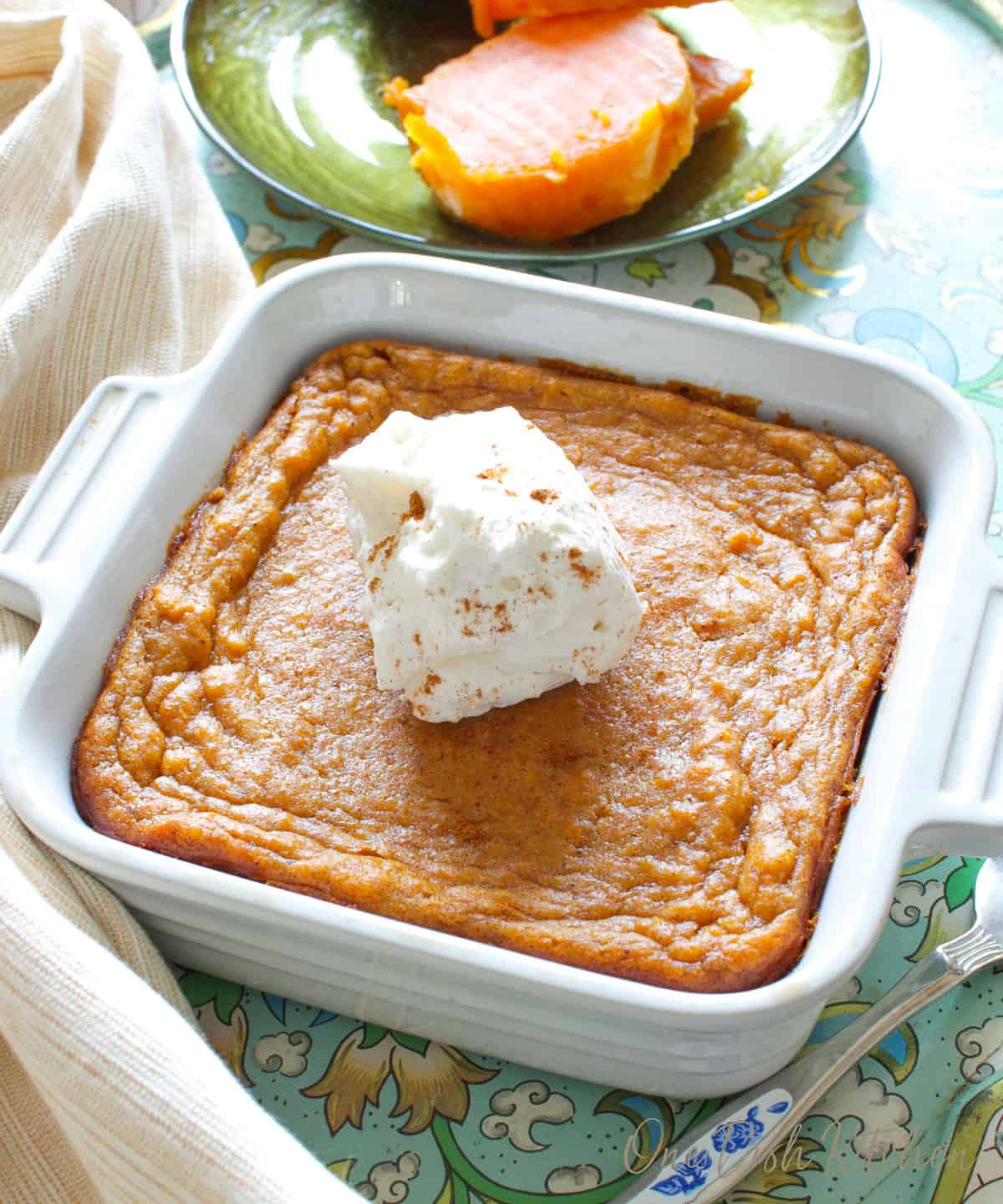 a small sweet potato pie in a square baking dish next to a plate of sliced sweet potatoes.